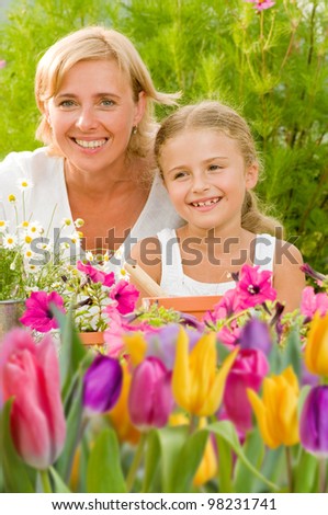 Spring garden, planting concept - mother with daughter planting flowers into the flowerpot