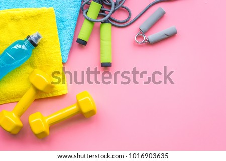 Fitness background. Equipment for gym and home. Jump rope, dumbbells, expander, mat, water on pastel pink background top view copy space