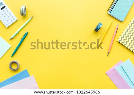 Scattered stationery on student\'s desk. Yellow background top view copy space