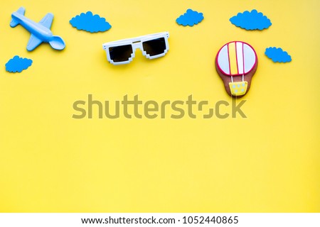 Airplan, air balloon toys and paper clouds for family traveling with child on yellow background top view mock-up