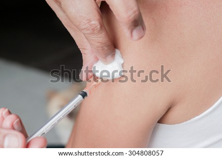 Asian woman is taking vaccine shot on her shoulder.