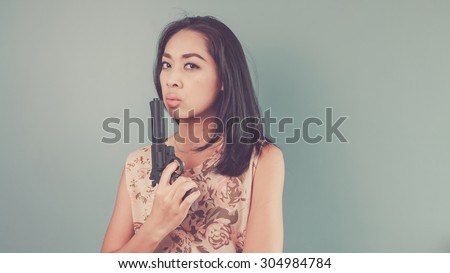 She is blowing gun smoke. Vintage, retro style of portrait of Asian woman in pink vintage dress on blue - green background.