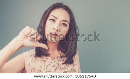 Thumb down sign. Vintage, retro style of portrait of Asian woman in pink vintage dress on blue - green background.