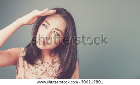 Hand cover the face to protect from bright light. Vintage, retro style of portrait of Asian woman in pink vintage dress on blue - green background.