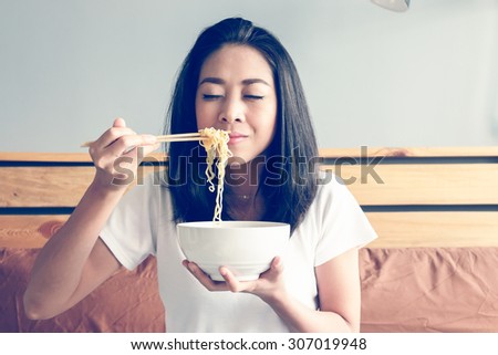 Smell the noodle with eyes closed. Asian girl eats instant noodle on the bed.