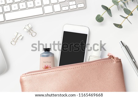 smartphone mock-up with rose gold clutch bag, cosmetics, office tools, keyboard and eucalyptus twigs on a white feminine styled desk - flat lay / top view