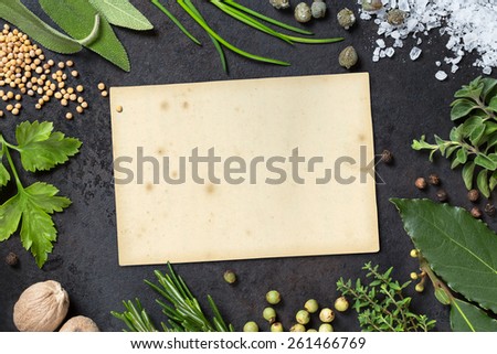 various herbs arranged as a frame on a dark metal tray, paper scrap with copyspace for your text