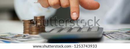 Male hand push key silver calculator is lying on desk cash dollar plots in home office setting. Calculation of family expenses social income population freelance irs situation growth research concept