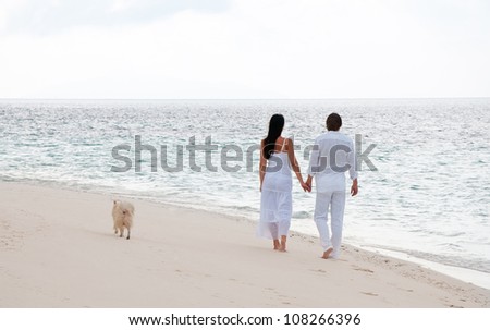 Picture of romantic young couple having a walking on the sea shore with dog