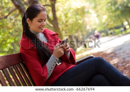 Young Caucasian woman with a cell phone, sitting in a park on a wooden bench, reading a SMS.