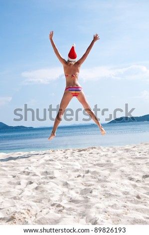 Young woman jump on the beach in santa\'s hat