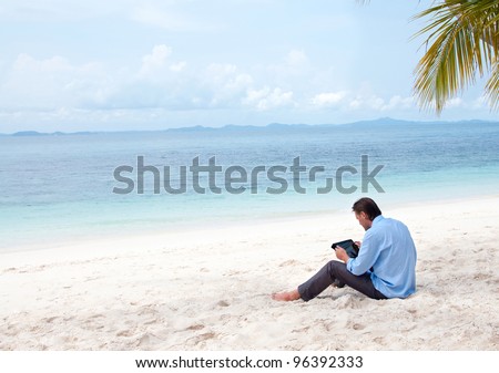 Business man sitting and working on the beach with tablet computer