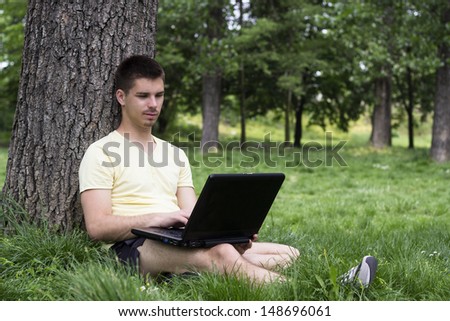 Studying with laptop in the park. Young man sitting and using laptop outdoors, looking at screen