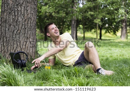Happy young male browsing internet on laptop. Young male watching something on laptop and smiling, in the park, spring/summer
