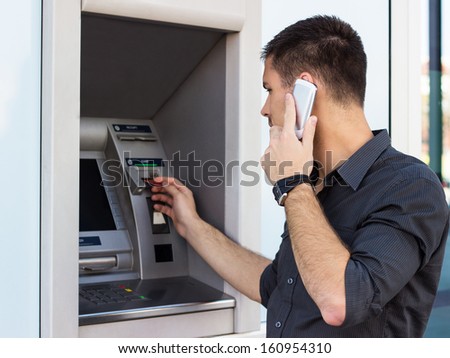 Handsome man talking on the phone and put his credit card at the atm