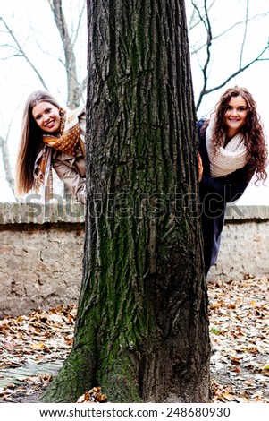 Two smiling friends behind a tree