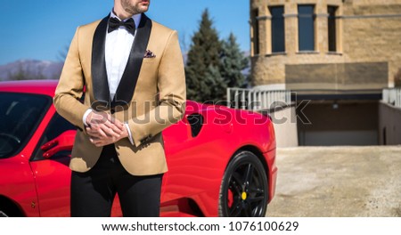 Man in custom tailored tuxedo, suit posing outdoors in front of expensive car