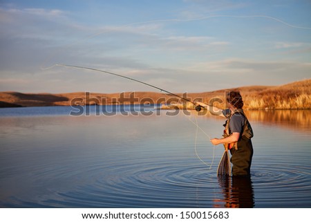 Fly fisherman casting in a lake in golden light.