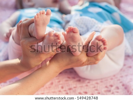 Legs newborns in parents hand. Twins lying on a pink blanket.