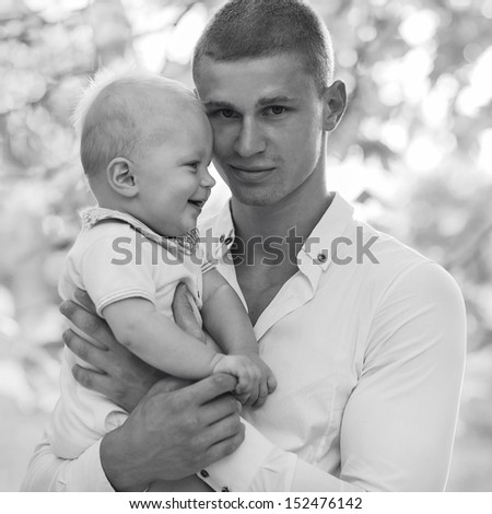 Black and white photo of his father and a small child. Father looks into the camera. The son looks at his father and laughs.