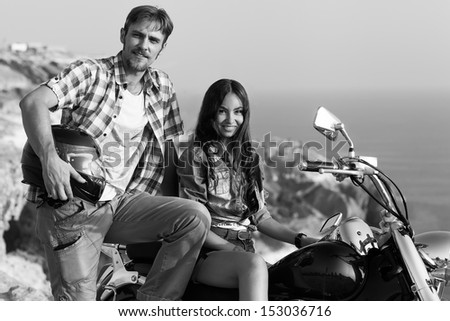 Stylish couple on a motorcycle. He put his foot on the exhaust pipe. She sits behind the wheel.