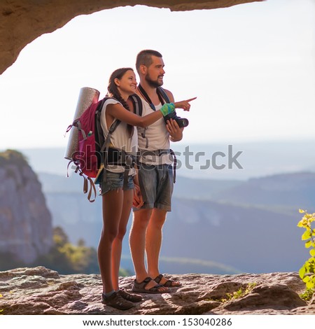 Two backpackers in mountains. Young couple examining the surroundings. The guy holding the camera, she shows off into the distance. Photos of the cave.