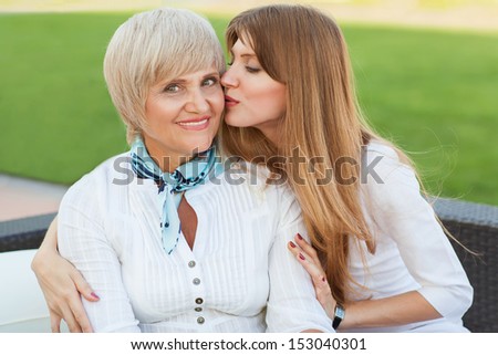 Adult mother and daughter in a cafe on the street. Daughter kissing smiling mother on the jowl.