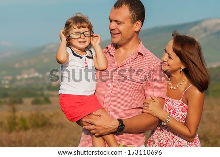 Happy mother, father and daughter in sunset. Daughter playing with glasses father.