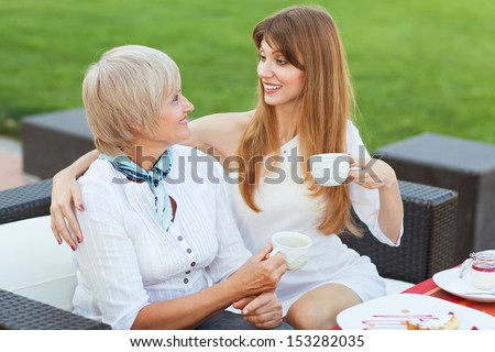 adult mother and daughter drinking tea or coffee and talking outdoors