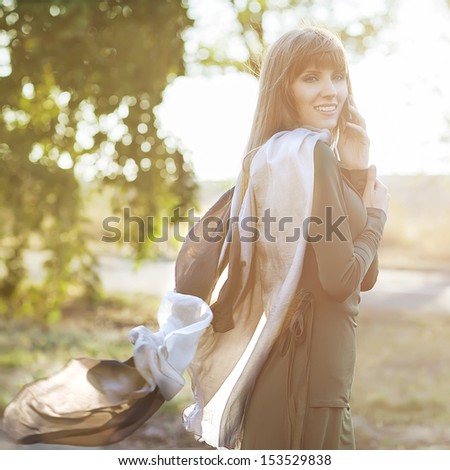 beautiful girl talking on the phone, her scarf is developing the wind in the setting sun.