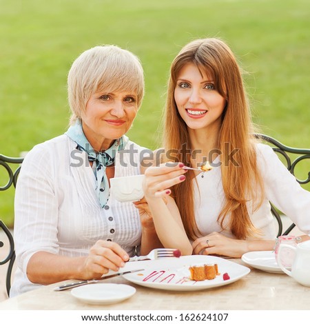 Adult mother and daughter drinking tea or coffee. They communicate sitting outside in a cafe.