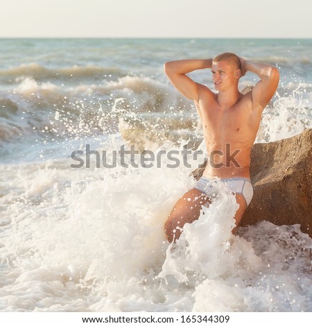Young handsome muscular man walking out of the water in a tropical beach wearing a bathing suit