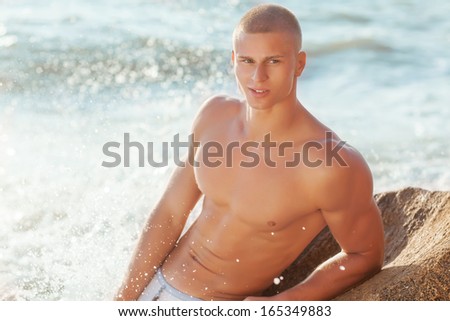 Portrait of a handsome young muscular man in swimtrunks with water ocean background