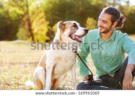 Man And Central Asian Shepherd Walk In The Park. He Keeps The Dog On The Leash.