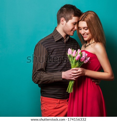 Portrait Of Young Couple In Love With Flowers Tulips Posing At Studio Dressed In Classic Clothes