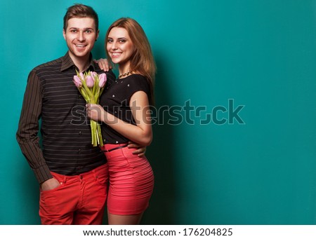 Portrait of young couple in love with flowers tulips posing at studio dressed in classic clothes