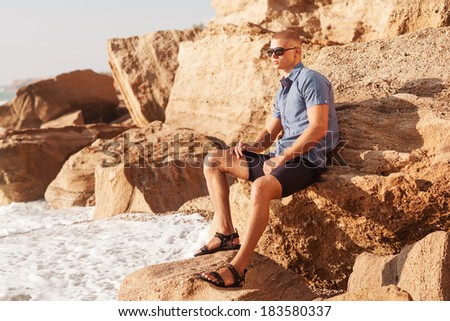 Fit worked-out man walking out of ocean onto beach with sky background and reflection in foreground