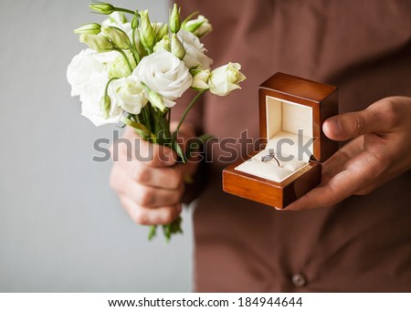 Happy man holding an engagement ring box in his hand and a bouquet of flowers
