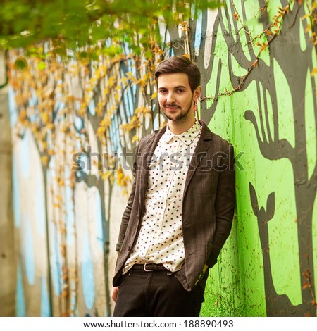 attractive young male model posing on green wall outdoors