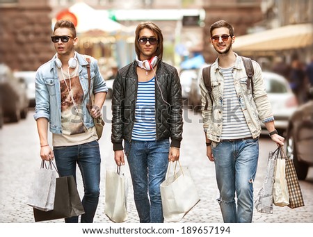 Fashion young guys go shopping with many colored shopping bags in their hands, watch purchase. In the background window dressing.