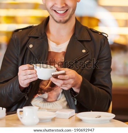 young hipster guy sitting in a cafe chatting and drinking coffee smiling