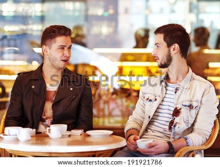 Two young hipster guy sitting in a cafe chatting and drinking coffee smiling