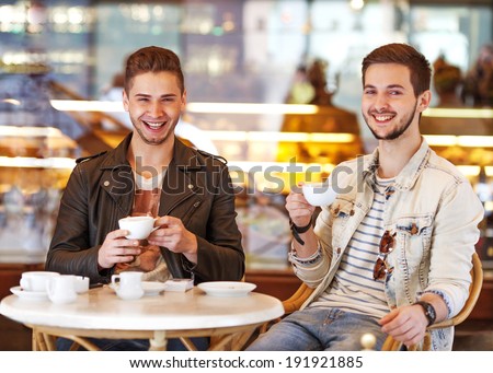 Two young hipster guy sitting in a cafe chatting and drinking coffee smiling