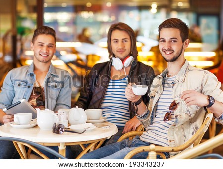 young hipster guys sitting in a cafe chatting and drinking coffee smiling and using tablet computer in cafe