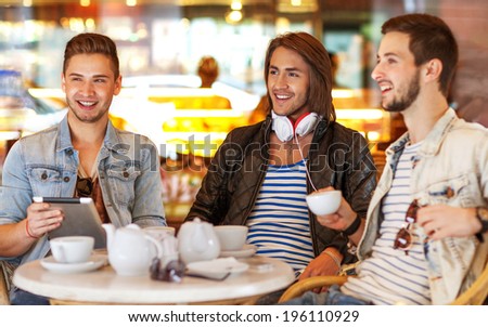 young hipster guys sitting in a cafe chatting and drinking coffee smiling and using tablet computer in cafe