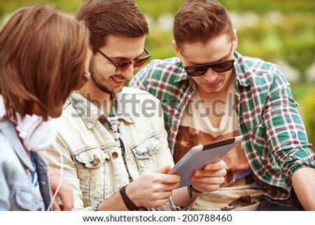 Three young men friends using tablet computer in park