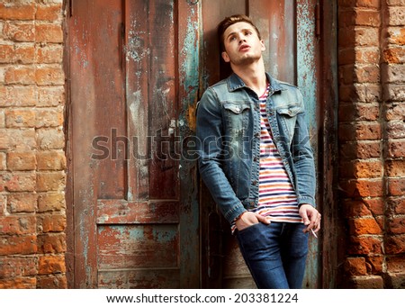 Hipster style guy. Fashion man standing near a wooden door and smoking