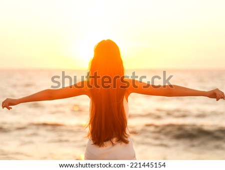 Free woman enjoying freedom feeling happy at beach at sunset. Beautiful serene relaxing woman in pure happiness and elated enjoyment with arms raised outstretched up. Asian Caucasian female model.