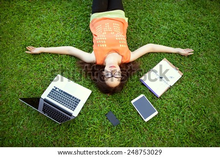 freelancer girl from the device: laptop, tablet, player, notebook, lying on the grass and working