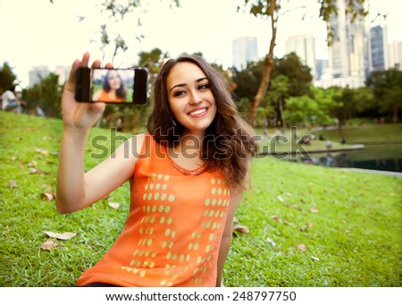 girl sitting in the park of Kuala Lumpur on the background of business centers and makes selfie, happy